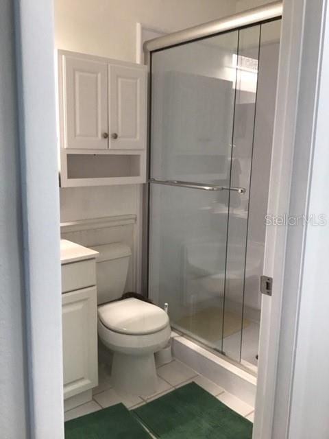 bathroom featuring walk in shower, vanity, toilet, and tile patterned flooring