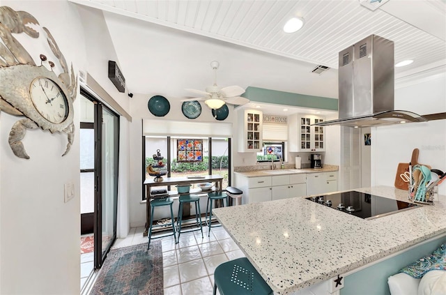 kitchen featuring light tile patterned floors, white cabinetry, light stone counters, black electric stovetop, and island range hood