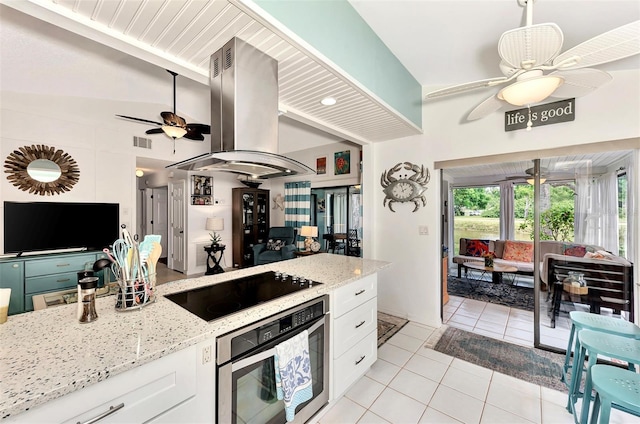 kitchen with light stone counters, island range hood, white cabinets, black electric cooktop, and oven