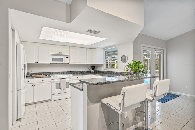 kitchen with white cabinetry, white appliances, a kitchen breakfast bar, and kitchen peninsula