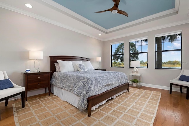 bedroom featuring crown molding, light hardwood / wood-style flooring, ceiling fan, and a tray ceiling