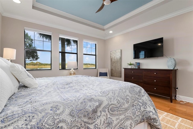 bedroom featuring crown molding, ceiling fan, a tray ceiling, and light hardwood / wood-style flooring