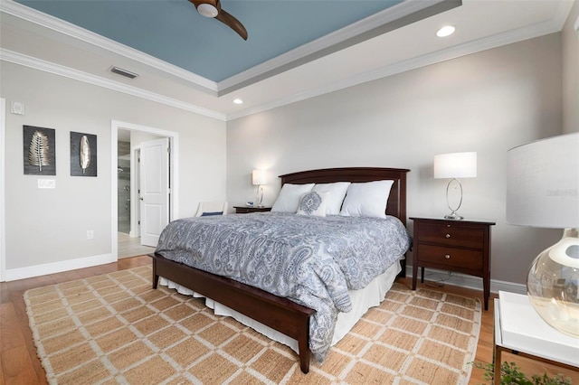 bedroom featuring a raised ceiling, wood-type flooring, ornamental molding, and ceiling fan