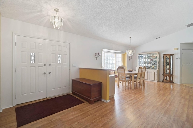 entrance foyer with an inviting chandelier, lofted ceiling, a textured ceiling, and light wood-type flooring