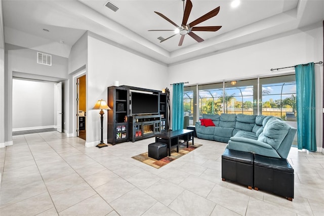 tiled living room featuring a towering ceiling, ceiling fan, and a tray ceiling