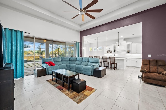 living room featuring light tile patterned flooring, ceiling fan, a healthy amount of sunlight, and a raised ceiling