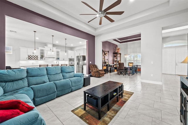 living room with light tile patterned flooring, ceiling fan, and a tray ceiling