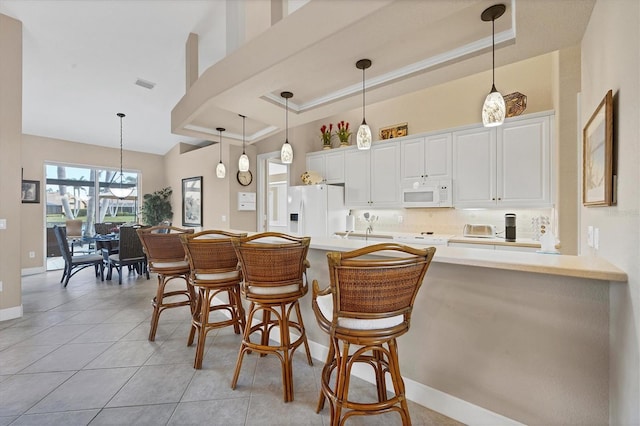 kitchen with white appliances, a breakfast bar, a towering ceiling, a tray ceiling, and white cabinets