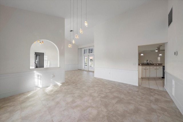 unfurnished living room with a ceiling fan, high vaulted ceiling, a sink, wainscoting, and a decorative wall