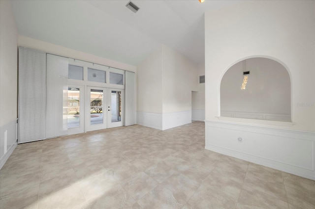 unfurnished room featuring visible vents, high vaulted ceiling, french doors, wainscoting, and a decorative wall