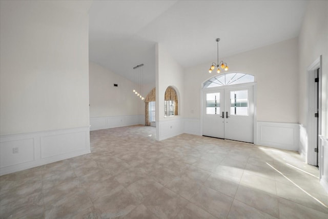 foyer entrance with french doors, lofted ceiling, a chandelier, and wainscoting