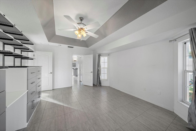 interior space with visible vents, baseboards, ceiling fan, light tile patterned flooring, and a raised ceiling