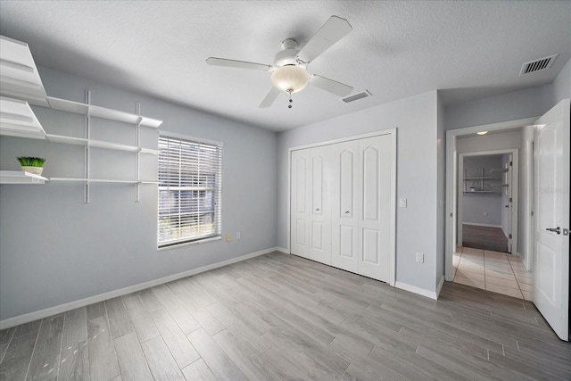 unfurnished bedroom featuring visible vents, a textured ceiling, baseboards, and wood finished floors