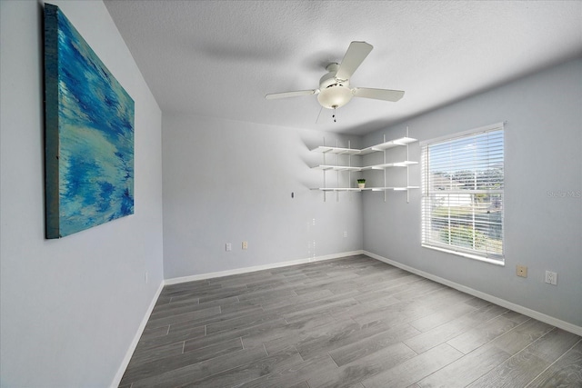 unfurnished room with a textured ceiling, a ceiling fan, baseboards, and wood finished floors