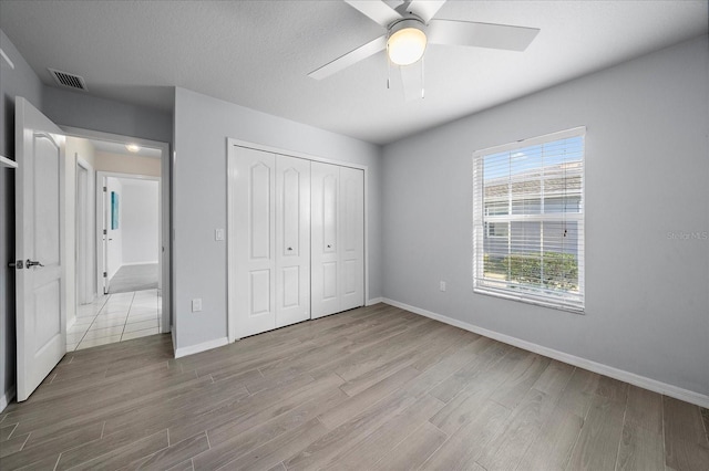 unfurnished bedroom featuring ceiling fan, a textured ceiling, light hardwood / wood-style floors, and a closet