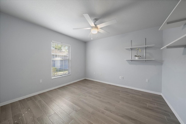 empty room featuring ceiling fan, baseboards, a textured ceiling, and wood finished floors