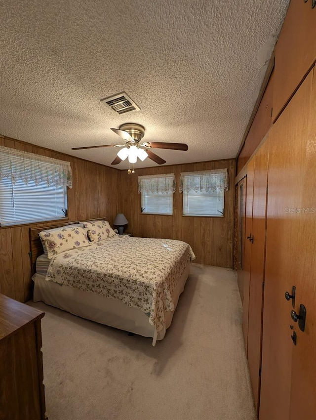 bedroom featuring ceiling fan, a textured ceiling, wooden walls, and light colored carpet