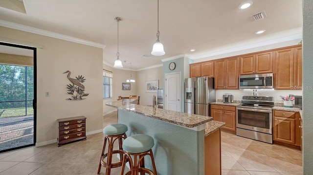 kitchen featuring a breakfast bar area, light stone counters, hanging light fixtures, a center island with sink, and appliances with stainless steel finishes