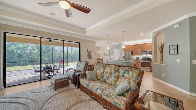 tiled living room with a raised ceiling, ornamental molding, and ceiling fan