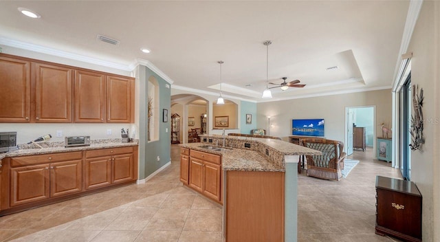 kitchen with decorative light fixtures, sink, a center island, a tray ceiling, and light stone countertops