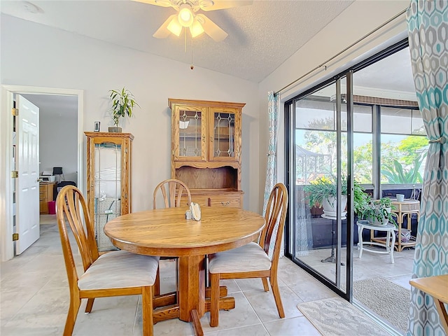 tiled dining room featuring ceiling fan, vaulted ceiling, and a textured ceiling