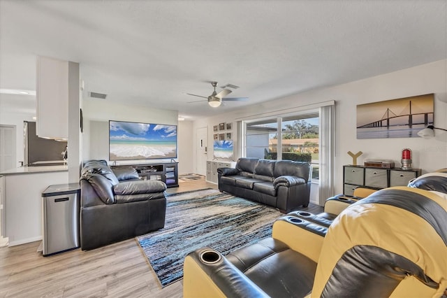 living room with ceiling fan, a textured ceiling, and light wood-type flooring