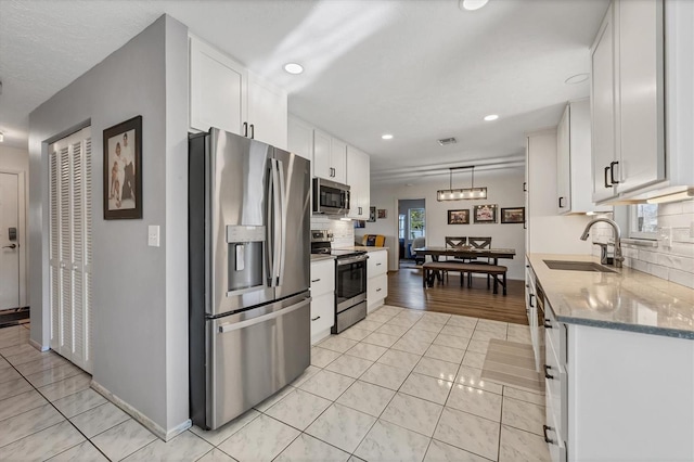 kitchen with sink, decorative light fixtures, appliances with stainless steel finishes, light stone countertops, and white cabinets