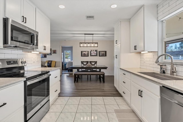 kitchen featuring sink, white cabinetry, hanging light fixtures, light tile patterned floors, and appliances with stainless steel finishes