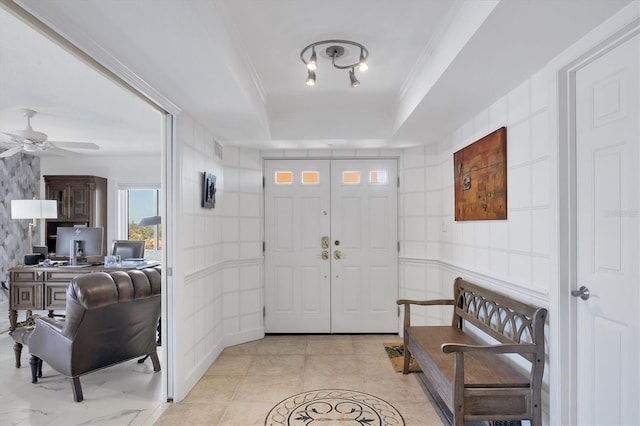 foyer entrance with ceiling fan, tile walls, a tray ceiling, ornamental molding, and light tile patterned flooring