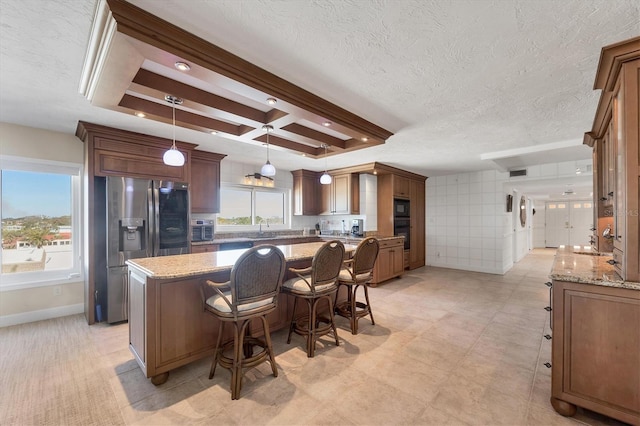 kitchen with a kitchen island, hanging light fixtures, coffered ceiling, black appliances, and light stone countertops