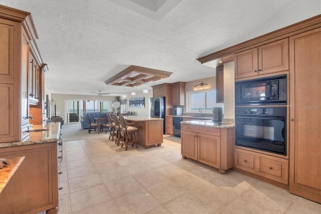 kitchen featuring a breakfast bar, a center island, a textured ceiling, light stone countertops, and black appliances