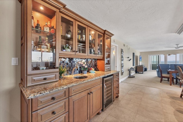 bar featuring tasteful backsplash, sink, beverage cooler, light stone counters, and a textured ceiling