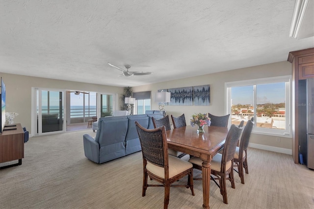 dining space featuring a water view, a healthy amount of sunlight, light carpet, and ceiling fan