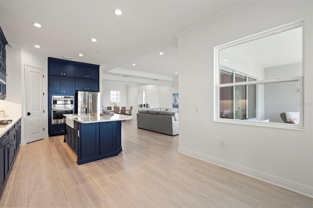 kitchen with blue cabinets, an island with sink, appliances with stainless steel finishes, and light hardwood / wood-style flooring