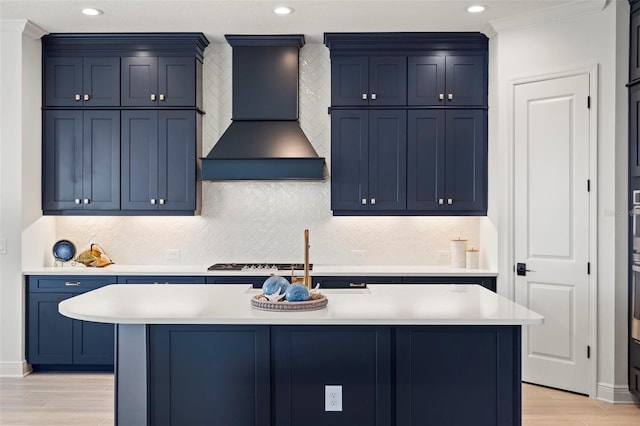 kitchen with light hardwood / wood-style flooring, blue cabinetry, premium range hood, a center island with sink, and stainless steel gas stovetop