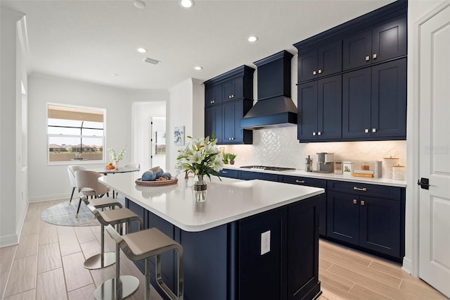 kitchen with blue cabinetry, a breakfast bar area, custom exhaust hood, a kitchen island, and backsplash