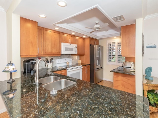 kitchen featuring sink, dark stone countertops, a tray ceiling, kitchen peninsula, and white appliances