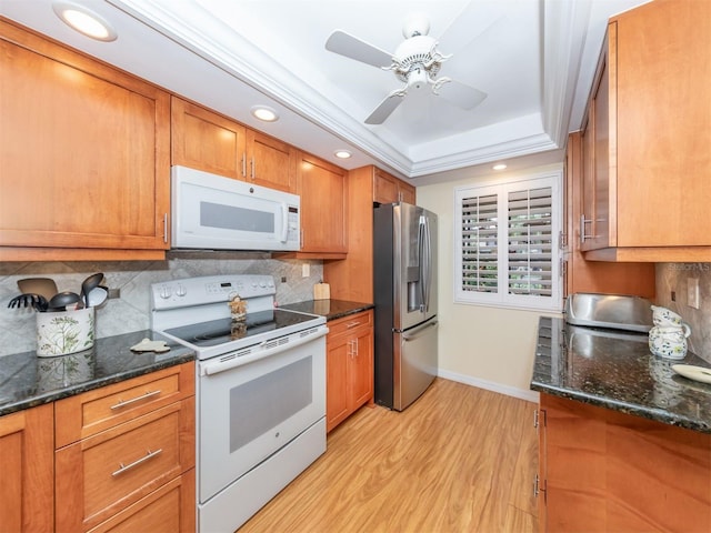 kitchen with white appliances, light hardwood / wood-style flooring, backsplash, a raised ceiling, and dark stone counters