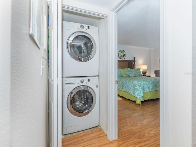 clothes washing area featuring wood-type flooring and stacked washing maching and dryer