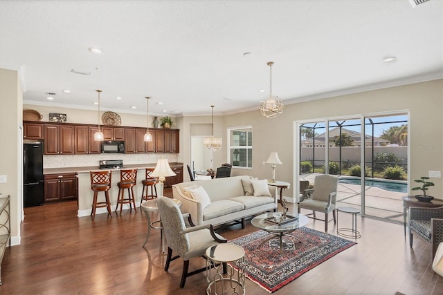 living room with dark wood-type flooring, ornamental molding, and a chandelier