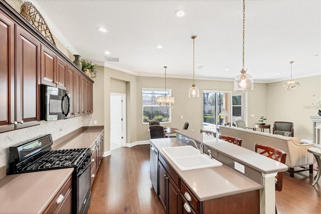 kitchen featuring sink, gas stove, hanging light fixtures, dark hardwood / wood-style flooring, and a kitchen island with sink