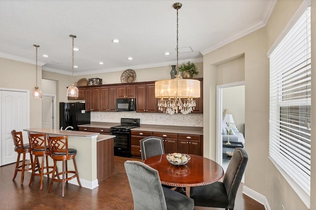 kitchen featuring pendant lighting, crown molding, a center island with sink, black appliances, and a kitchen bar