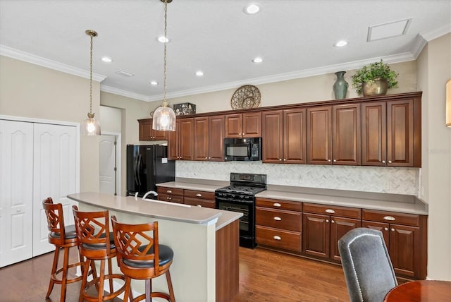 kitchen featuring a breakfast bar, wood-type flooring, hanging light fixtures, black appliances, and a center island with sink