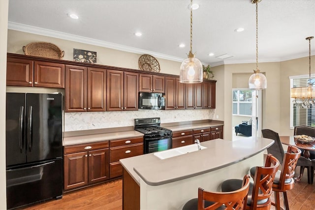 kitchen featuring pendant lighting, a kitchen breakfast bar, an island with sink, and black appliances