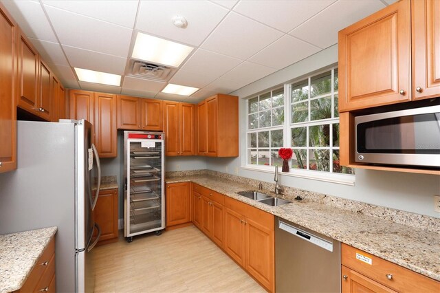 kitchen with wine cooler, sink, light stone counters, a paneled ceiling, and stainless steel appliances