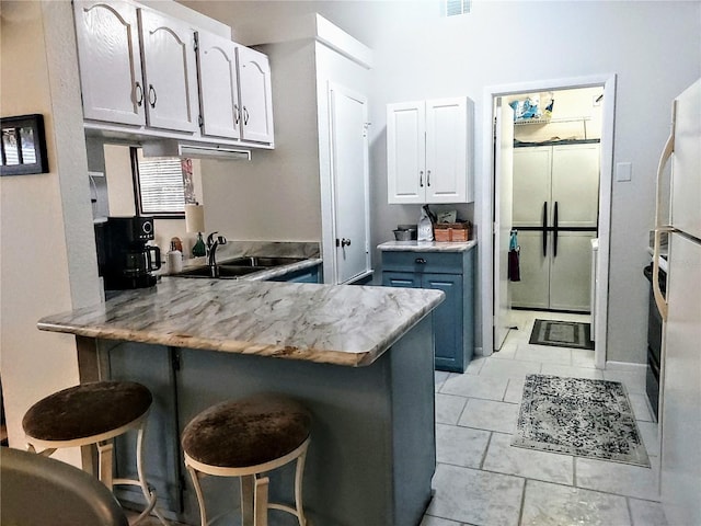 kitchen featuring sink, blue cabinetry, a kitchen breakfast bar, white cabinets, and kitchen peninsula