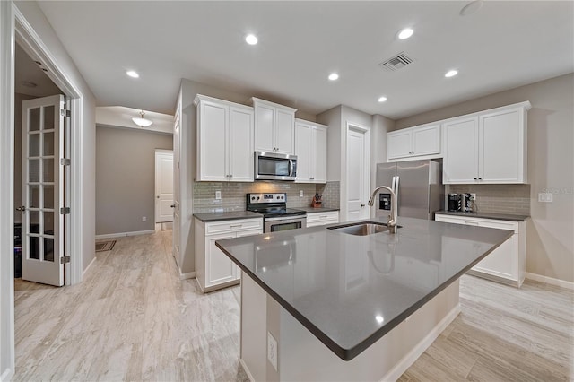 kitchen with sink, a kitchen island with sink, white cabinetry, stainless steel appliances, and decorative backsplash