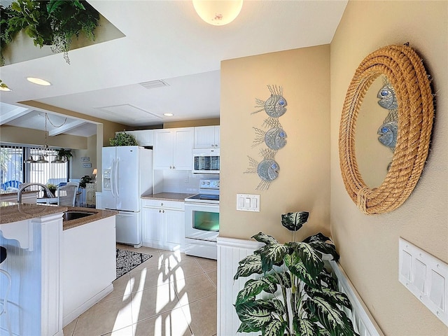 kitchen with light tile patterned floors, sink, white appliances, hanging light fixtures, and white cabinets