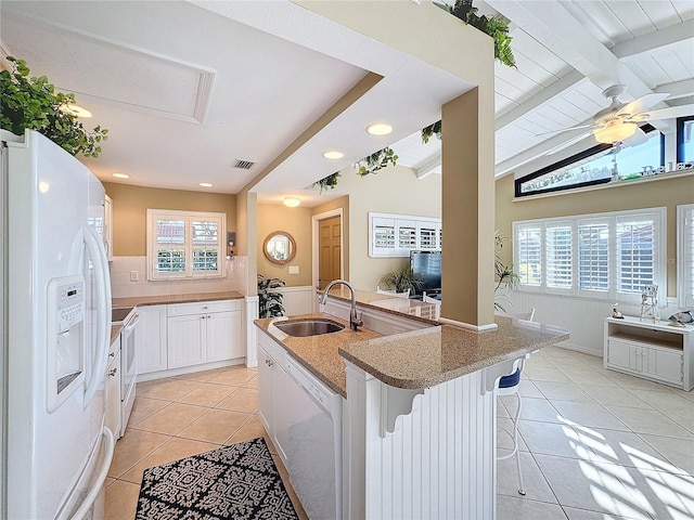 kitchen featuring sink, a breakfast bar area, white cabinets, light tile patterned floors, and white appliances