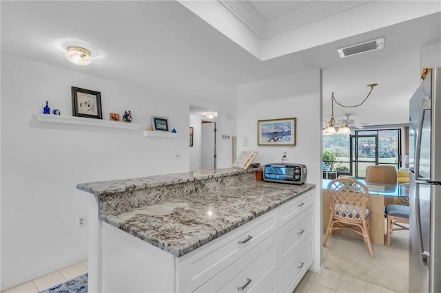 kitchen with white cabinetry, light stone countertops, light tile patterned floors, and stainless steel fridge